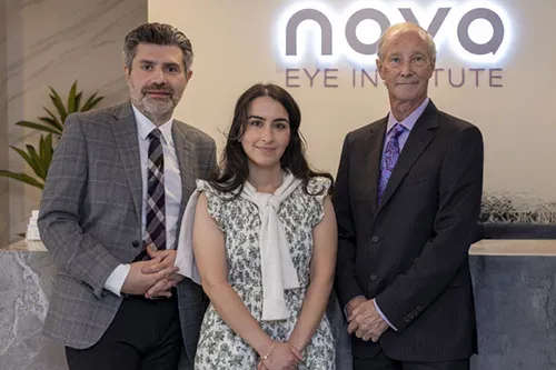 Three professionals pose together at the Nova Eye Institute reception desk, smiling for the camera.