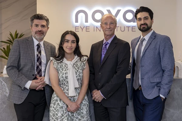 Group of four professionals posing at a reception desk in front of a Nova Eye Institute sign in a clinic lobby.